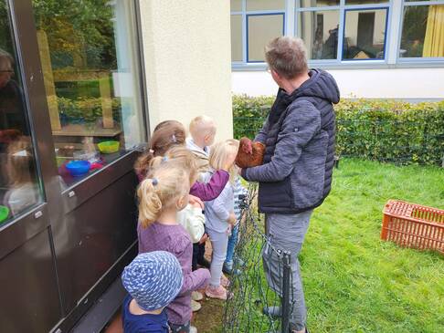 Ein paar Kinder stehen bei einem Erwachsenen der ein Huh auf dem Arm hat.