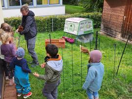 Ein paar Kinder stehen bei einem Erwachsenen der ein Huh auf dem Arm hat.