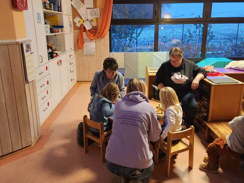 Einige Kinder mit Erwachsenen in einem Raum.