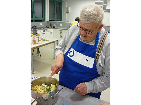 Mann hält kleinen Löffel über Kochtopf.