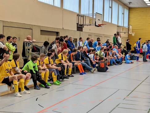 Sportler sitzen in einer Halle am Spielfeldrand.