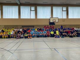 Mehrere Fussballteams sitzen in der Halle am Rand.
