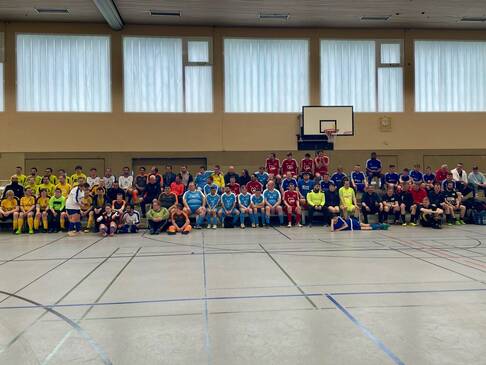 Mehrere Fussballteams sitzen in der Halle am Rand.