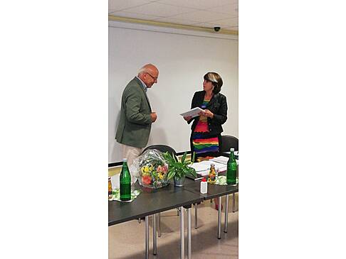 Eine Frau steht vor einem Mann und hält ein Geschenk in der Hand.