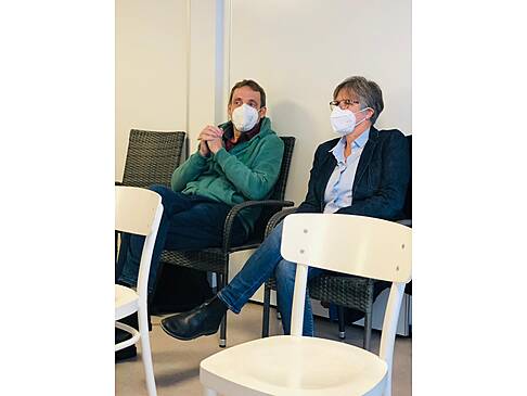 Ein Mann und eine Frau sitzen mit Maske in einem Raum.