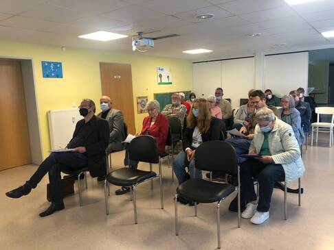 Viele Menschen sitzen in einem Raum und folgen einer Präsentation an der Wand