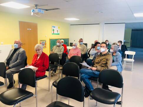 Viele Menschen sitzen in einem Raum und folgen einer Präsentation an der Wand