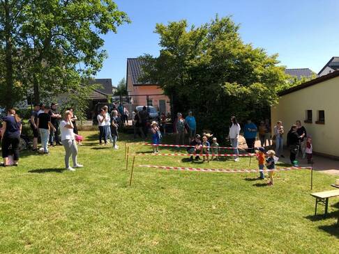 Erwachsene und Kinder draussen auf einer Wiese, Bereiche sind mit Flatterband abgetrennt.