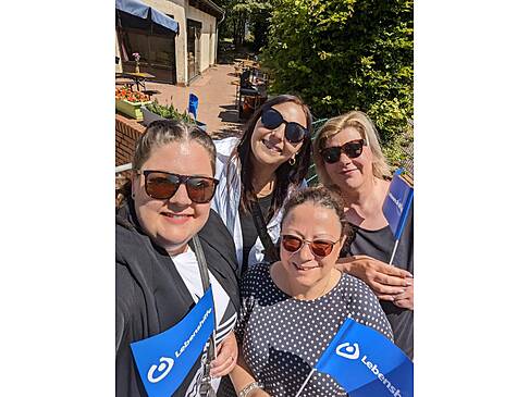 Vier Frauen mit Sonnenbrille und Lebenshilfefahnen stehen in der Sonne.