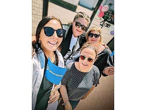 Vier Frauen mit Sonnenbrille und Lebenshilfefahnen stehen in der Sonne und lächeln..