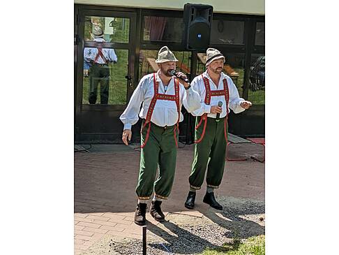 Zwei Männer in Tracht stehen in der Sonne und einer hält sich ein Mikrofon vor den Mund.