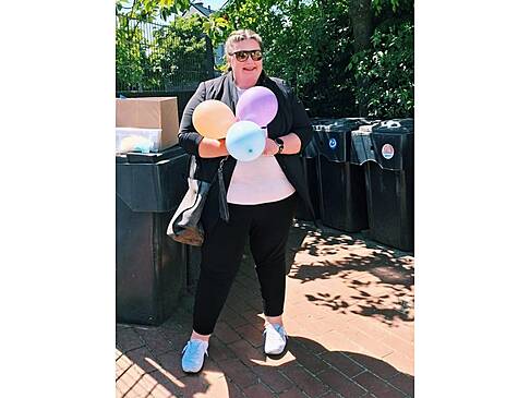 Eine Frau mit Sonnenbrille steht in der Sonne und hält Luftballons.