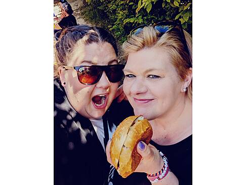 Zwei Frauen draussen, eine hält ein Bratwurstbrötchen in der Hand.