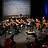 Ein Orchester auf der Bühne, sitzend.