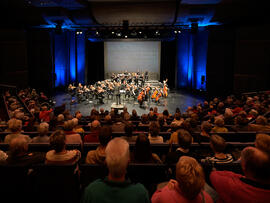 Eine Saalaufnahme, mit Puplikum und einem Orchester auf der Bühne.