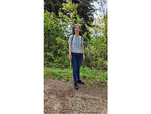 Eine Frau im Wald mit Müllgreifer in der Hand.