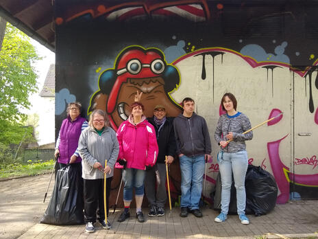 Sechs Personen stehen beisammen mit Mülltüte und Müllgreifer.