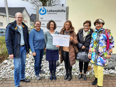 6 Personen stehen zusammen, zwei haben einen Scheck in der Hand.
