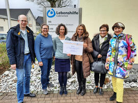 6 Personen stehen zusammen, zwei haben einen Scheck in der Hand.