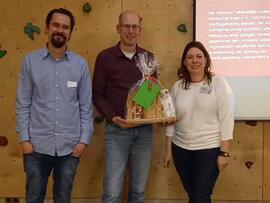 Auf einem Foto sieht an Thorbjörn Köpp, Sven Sieburg mit einem Geschenk und Stefanie Schröder