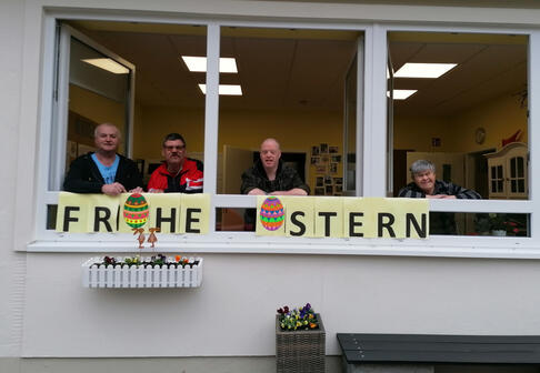 Vier Männer stehen am offenen Fenster mit den Worten davor, frohe Ostern.