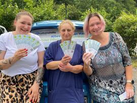 Drei frauen stehen hinter einem Auto und halten Karten hoch.