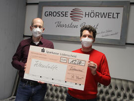 Zwei Männer halten einen Scheck über 1200€ in den Händen