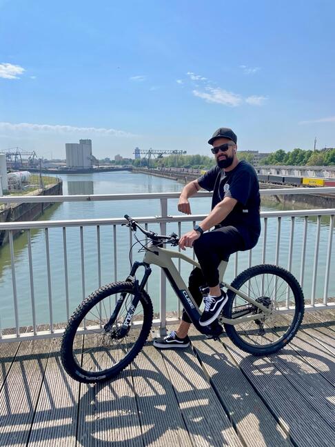 Herr Messam auf einem Fahrrad an einem Fluss