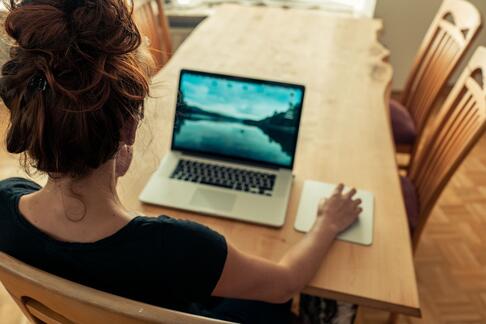 Eine Person sitzt am Tisch und hat eine PC Maus in der Hand.