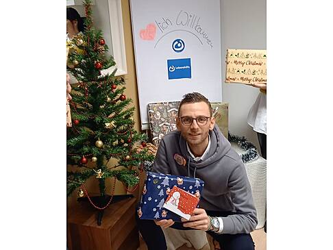 Ein Mann hockt neben einem Weihnachtsbaum mit Geschenken in der Hand.