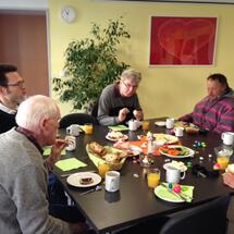 Menschen aus der Tagesbetreuung beim gemeinsamen Frühstück. Der Tisch ist reich gedeckt.