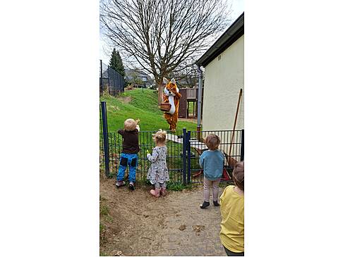 Kinder im Garten winken dem Hasen zu.