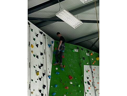 Ein junger Mann ganz oben an der Kletterwand.