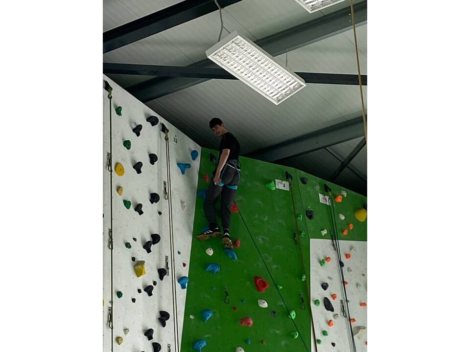 Ein junger Mann ganz oben an der Kletterwand.