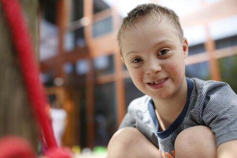 Ein Kind hockt, daraussen auf dem Boden und lächelt.