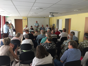 Es findet eine Mitgliederversammlung statt, bei der die Mitglieder einem Redner zuhören.