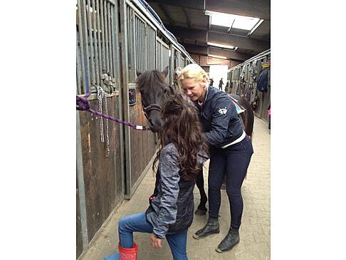 Frau und Mädchen stehen neben einem dunklen Pferd im Stall.