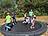 Eine Gruppe Kinder springt ausgelassen auf einem großen Trampolin im Garten. Sie bewegen sich voller Freude und Energie an einem sonnigen Tag.