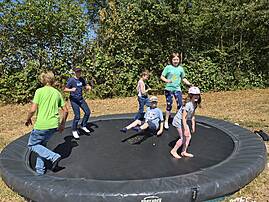 Eine Gruppe Kinder springt ausgelassen auf einem großen Trampolin im Garten. Sie bewegen sich voller Freude und Energie an einem sonnigen Tag.