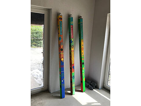 Drei lange Balken stehen bemalt gegen eine Wand.
