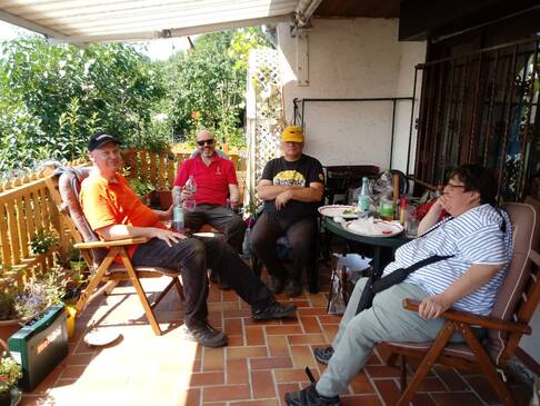 Vier Personen sitzen auf einer Terasse überwiegend im Schatten.
