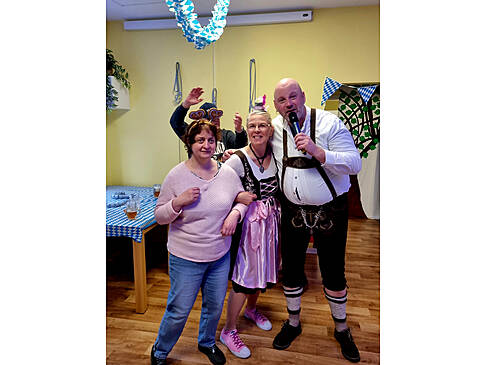 Ein Mann mit einem Mikrofon in der Hand hakt sich bei zwei Frauen ein.