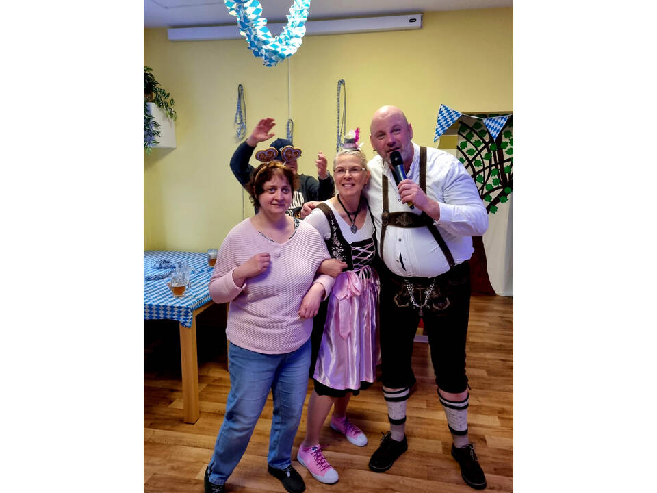 Ein Mann mit einem Mikrofon in der Hand hakt sich bei zwei Frauen ein.