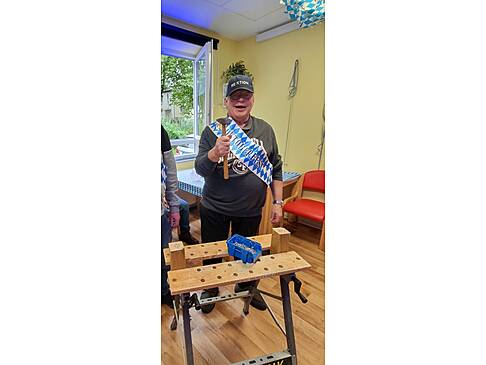 Ein Mann mit einem Hammer in der Hand, einem Kappi und einer blau weissen Scherpe.