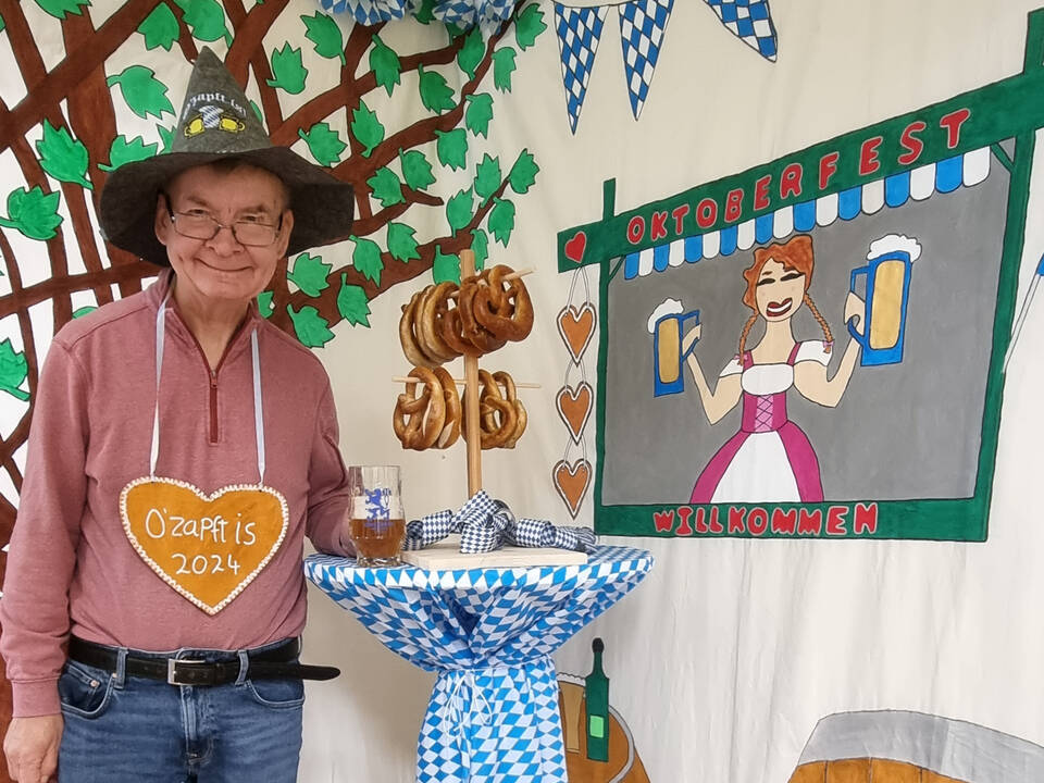 Ein Mann mit einem Lebkuchenherz neben einem Stehtisch mit Brezeln.