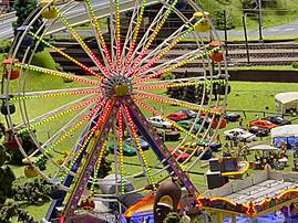 Ein bunt beleuchtetes Riesenrad steht in einer detailreichen Modellwelt mit Straßen, Schienen, Autos und Häusern. Die Gondeln sind in verschiedenen Farben gestaltet.