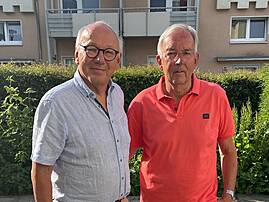 Dr. Wolfgang Schröder (links), 1. Vorsitzender des Aufsichtsrats der Lebenshilfe Lüdenscheid – Märkischer Kreis e.V., steht neben Reinhard Merkschien, der nach langjähriger Tätigkeit als 2. Vorsitzender verabschiedet wurde; beide stehen auf einem Pflasterhof vor einer Hecke.