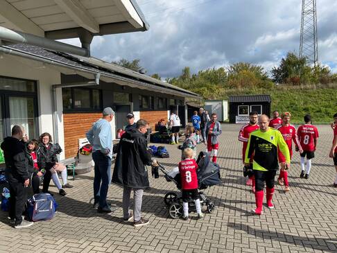 Personen gehen über einen Platz neben dem SPielfeld.