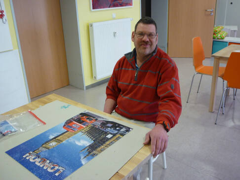 Ein Mann sitzt vor einem fertigen Puzzle am Tisch.