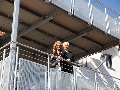 EIne Frau und eine Mann stehen auf einem Balkon in der Sonne.
